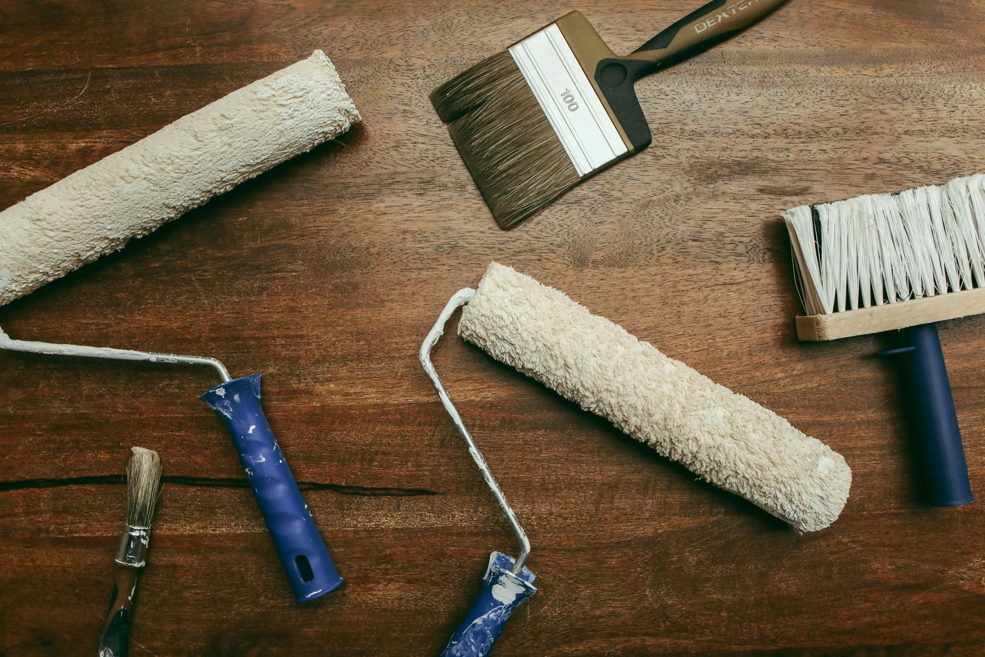 Top view of various painting tools including rollers and brushes laid out on a wooden surface.